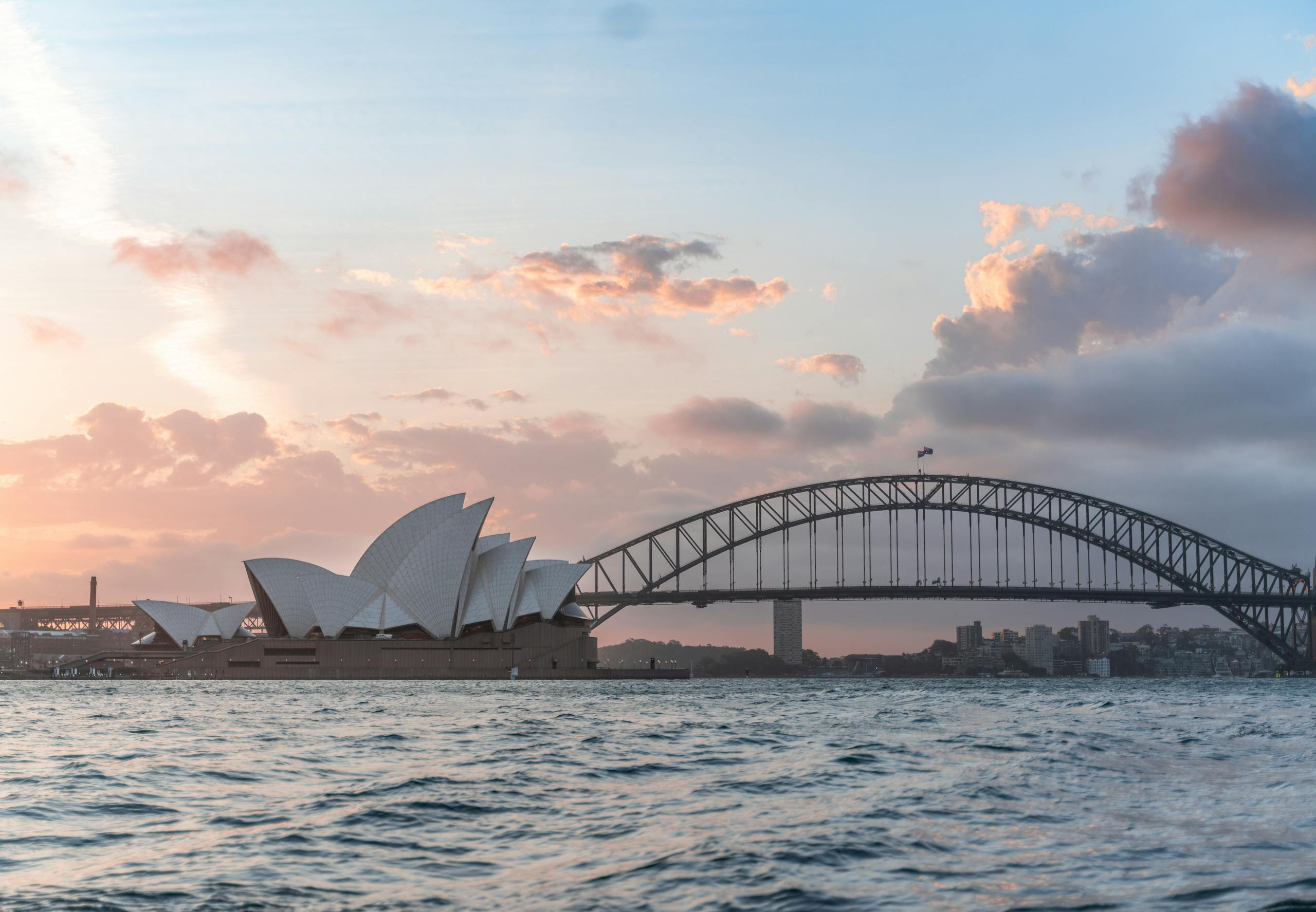 Amazing cityscape of Sydney with famous Opera House and arched Harbour Bridge connecting districts against picturesque cloudy sunset sky